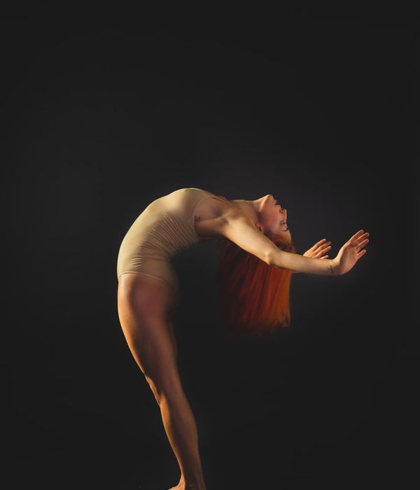 Woman in activewear performing a fluid cardio movement in a minimalist dark studio.